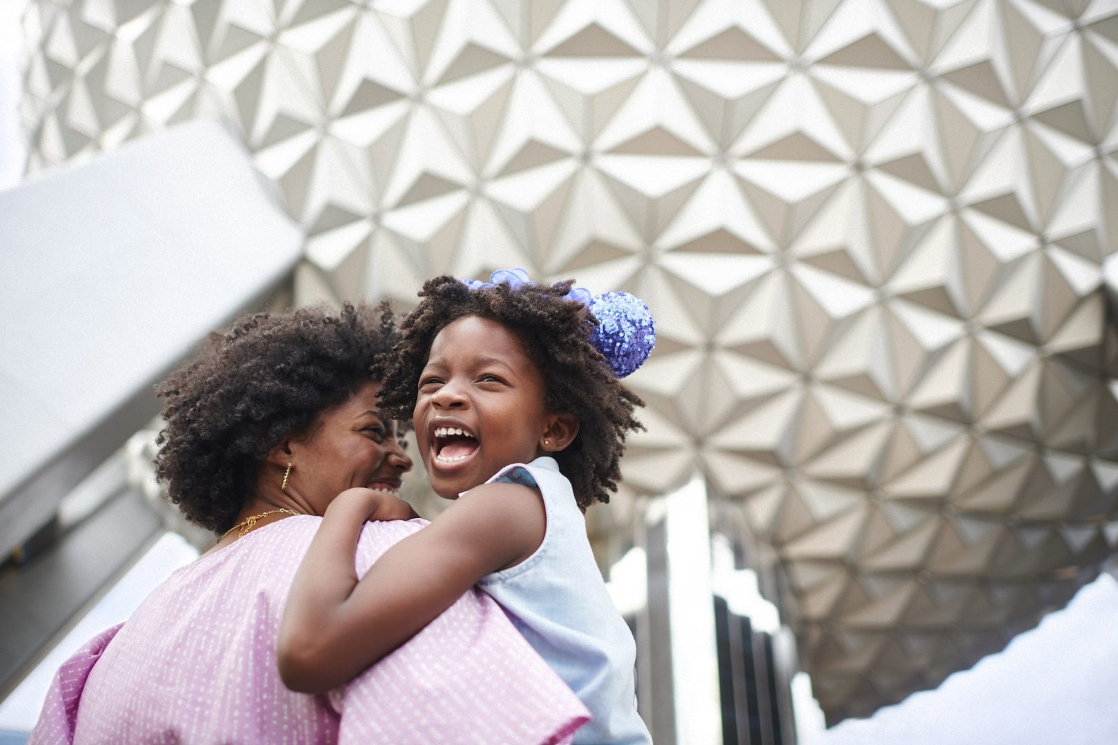 A joyful girl in a blue dress smiles while being held by a woman.