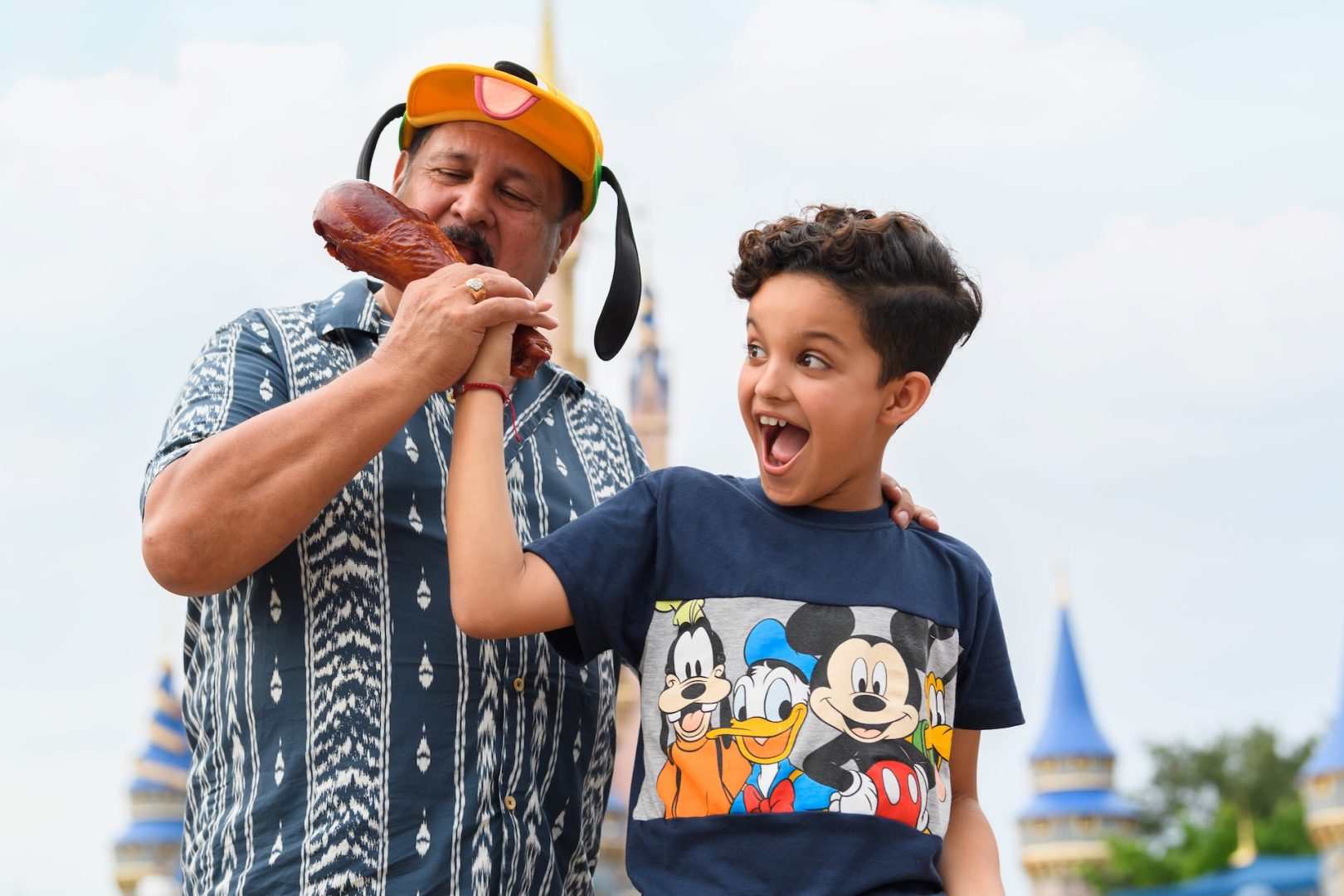 Man and boy smiling, holding a turkey leg at Disney World.