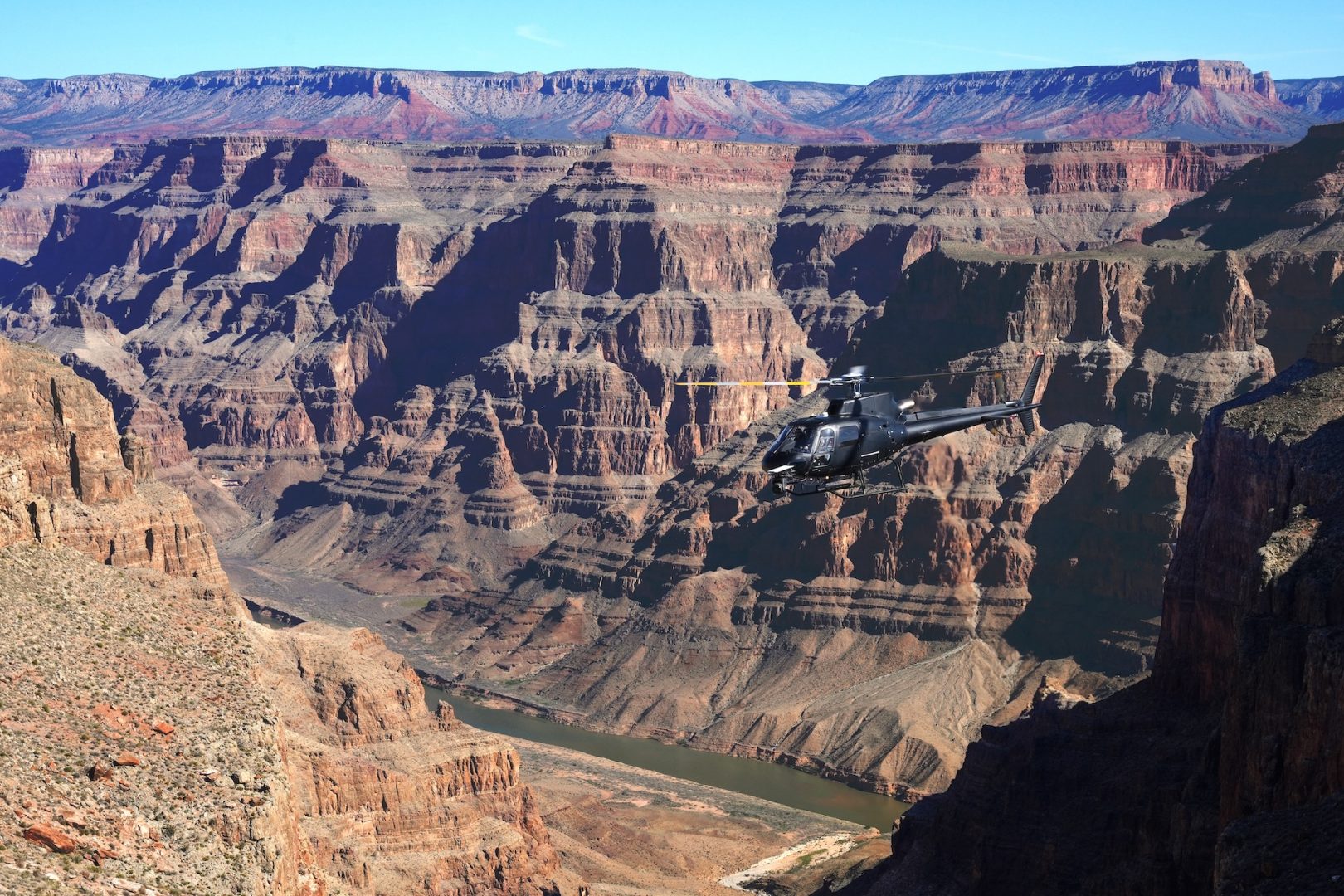 Helicopter flying over the Grand Canyon with rocky cliffs and river below.