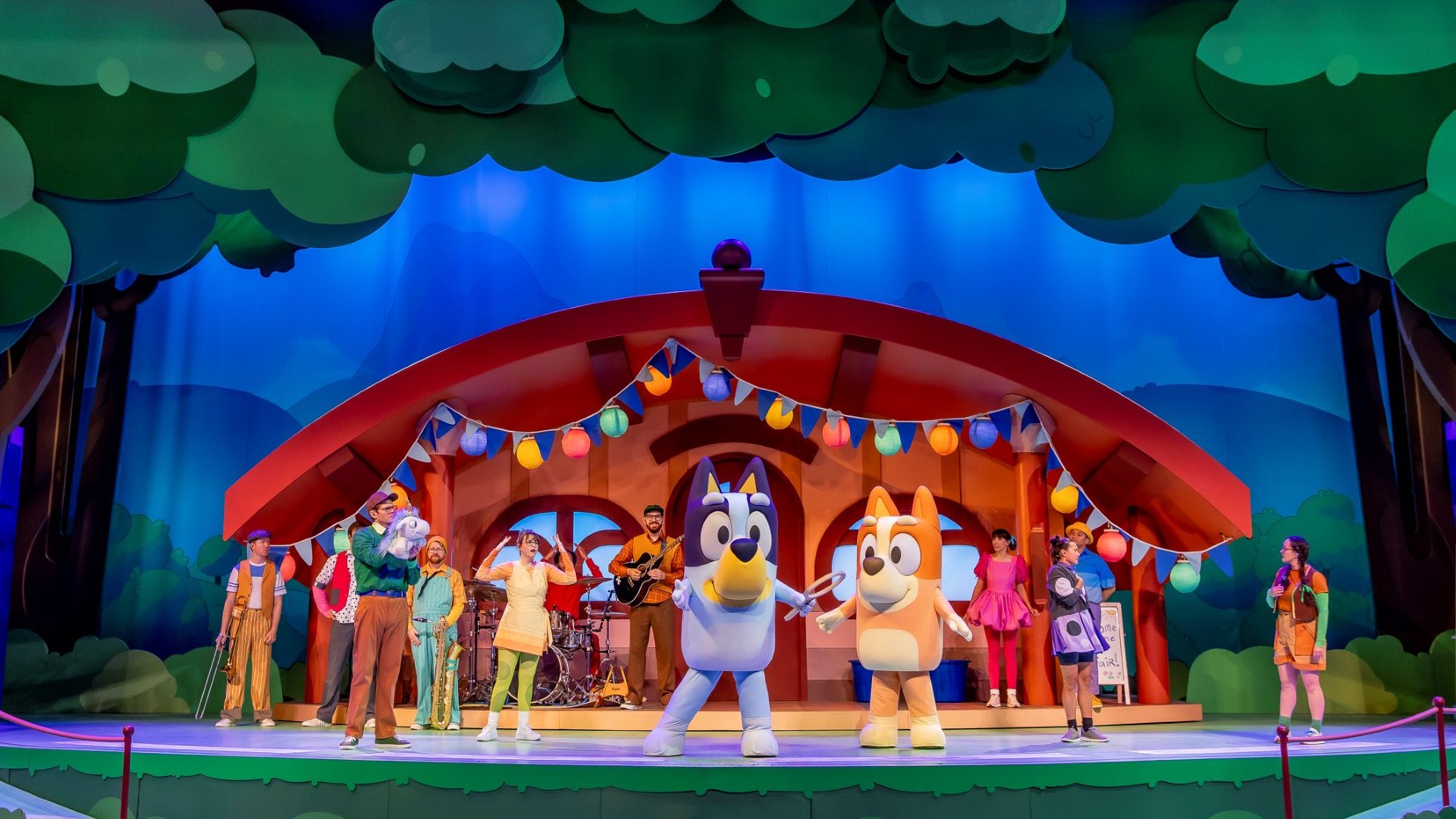 Bluey and Bingo perform on stage with colorful decorations and musicians.