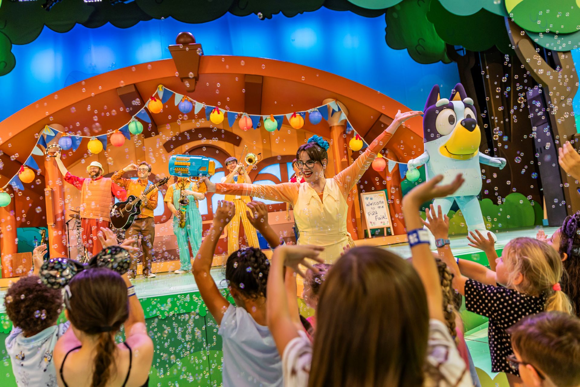 Children enjoying a performance with bubbles, music, and characters on stage.