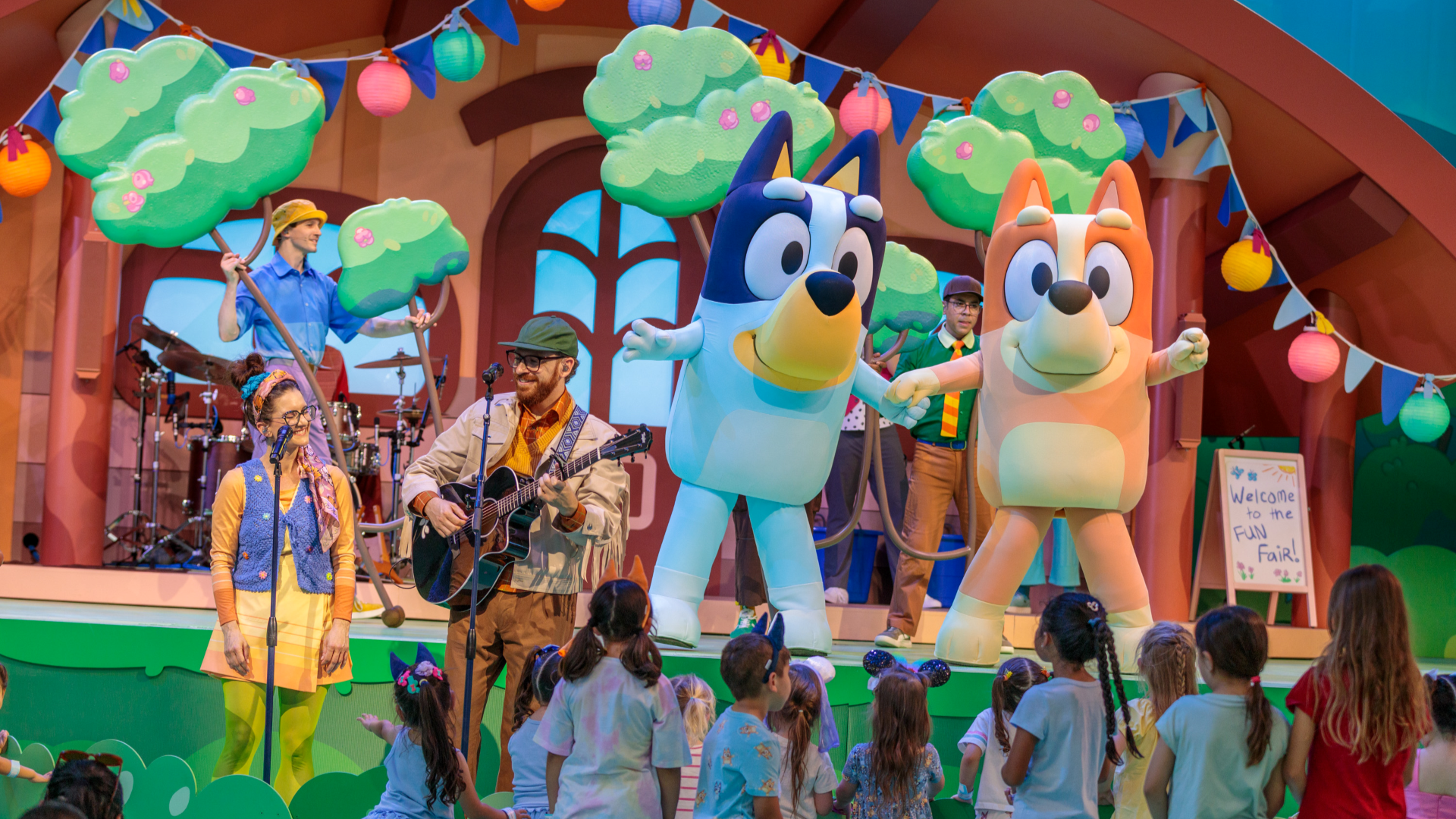 Bluey characters perform on stage, surrounded by children and colorful decorations.