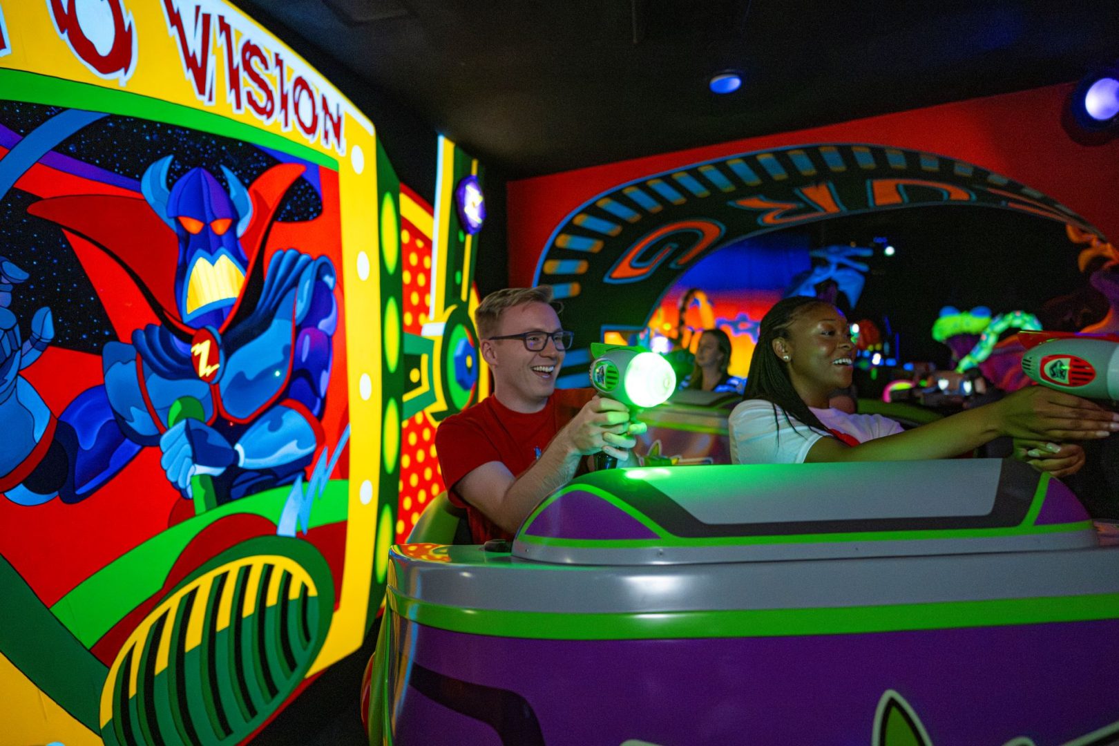 Two riders aiming laser guns in a colorful, animated attraction.