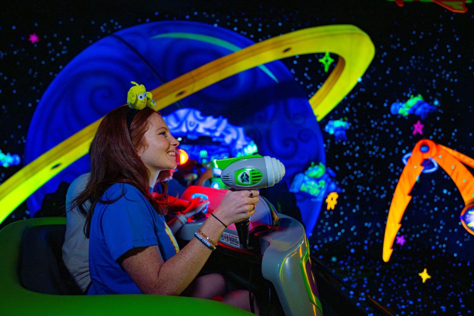 A woman smiles while aiming a toy blaster in a colorful space-themed ride.