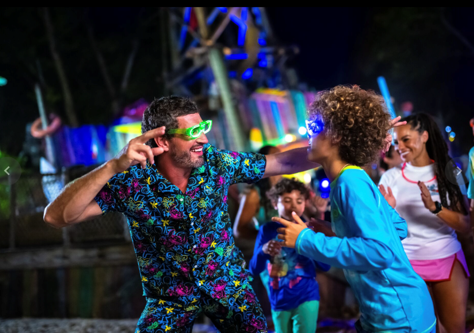 People dancing in colorful outfits with glowing accessories at a nighttime event.