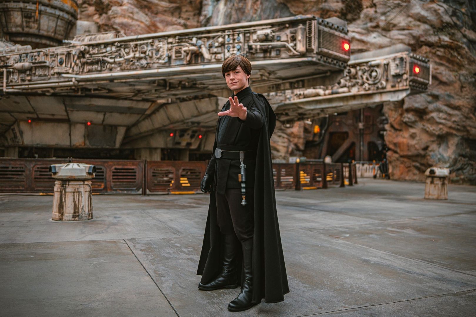Luke Skywalker in a black cloak poses near the Millennium Falcon.