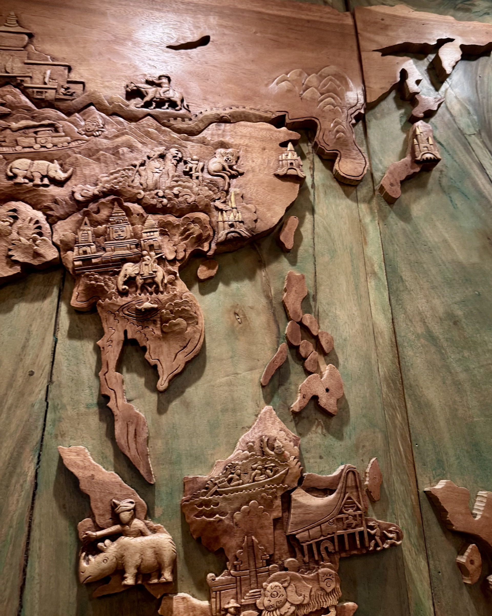 Carved wooden map of Asia featuring animals and landmarks.