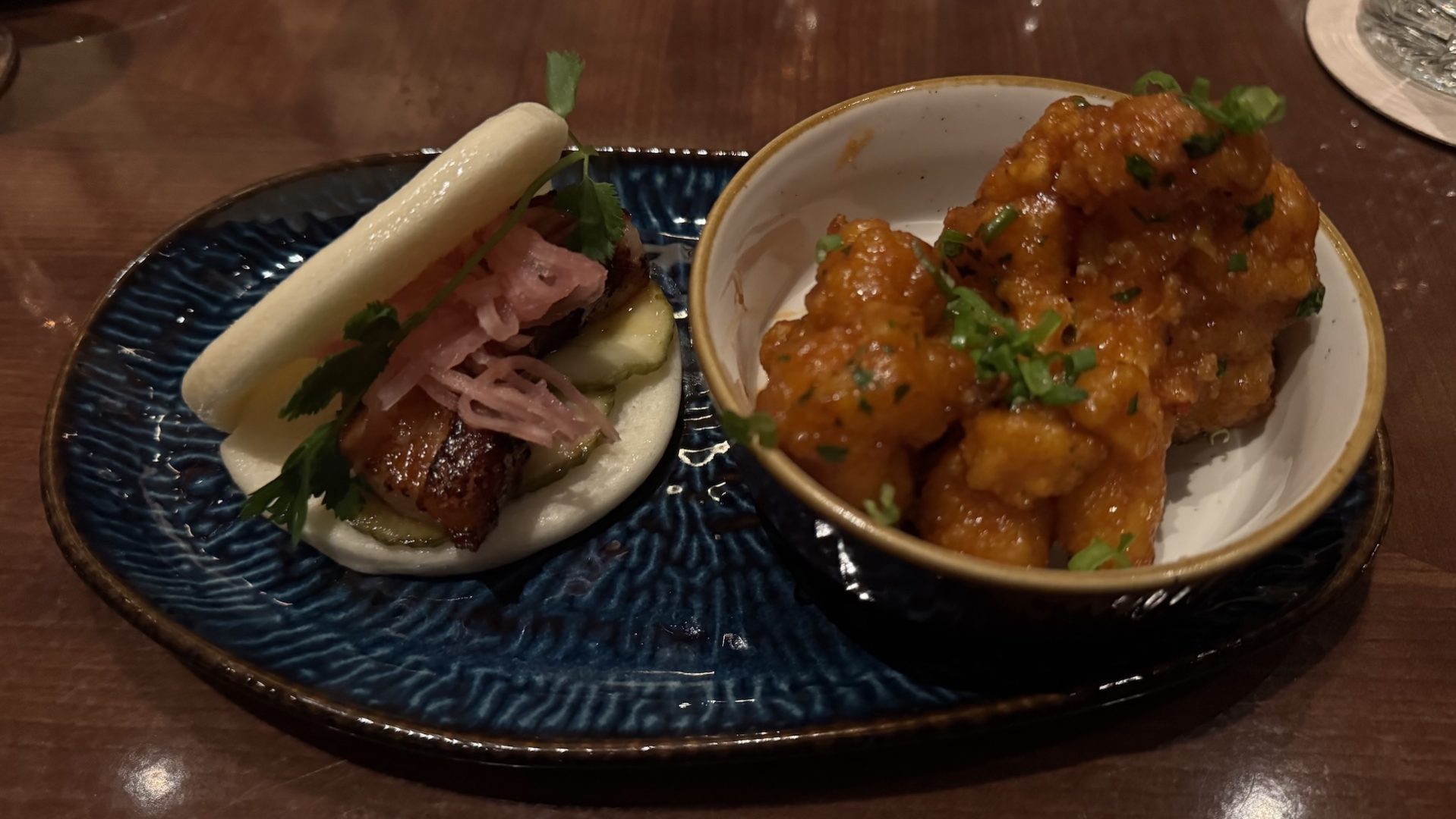 Plate with bao bun, pickled onions, and spicy chicken bites.