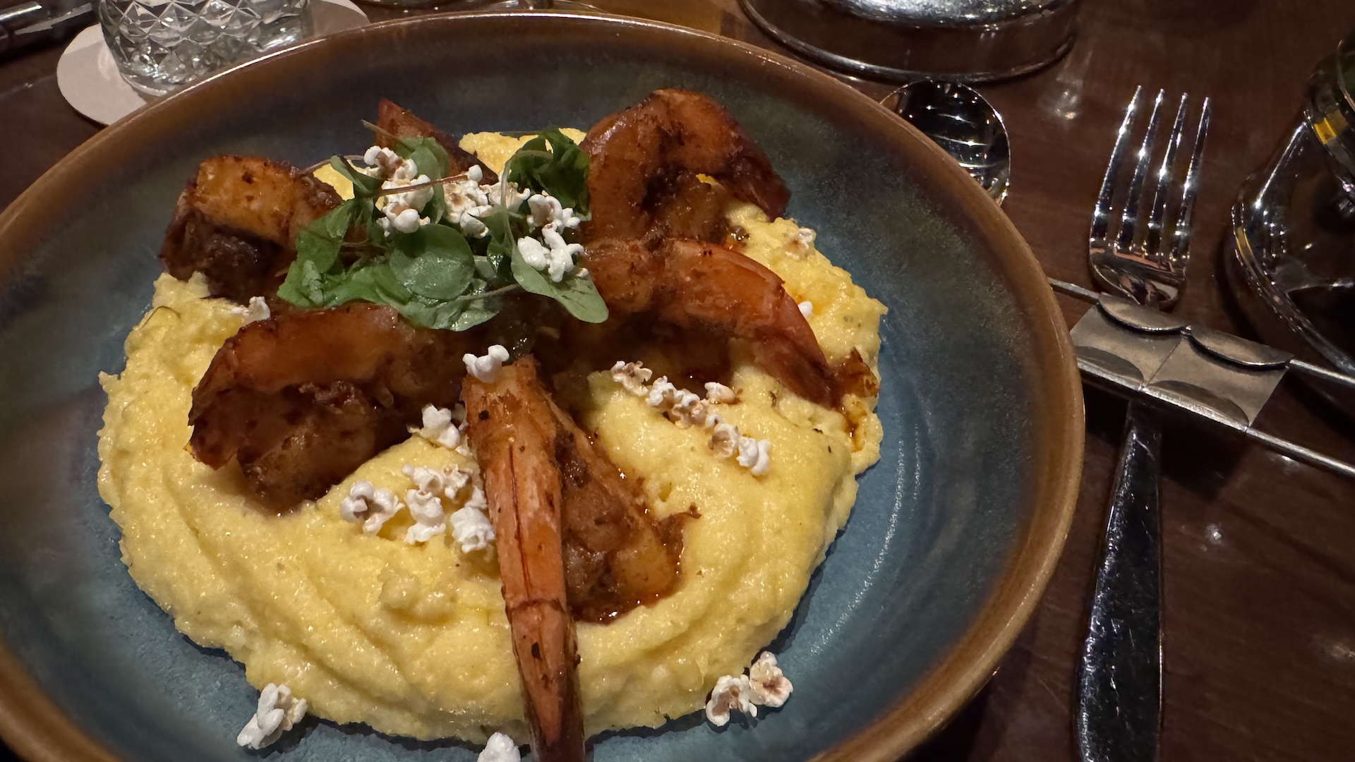 Shrimp atop creamy polenta garnished with greens and popcorn.