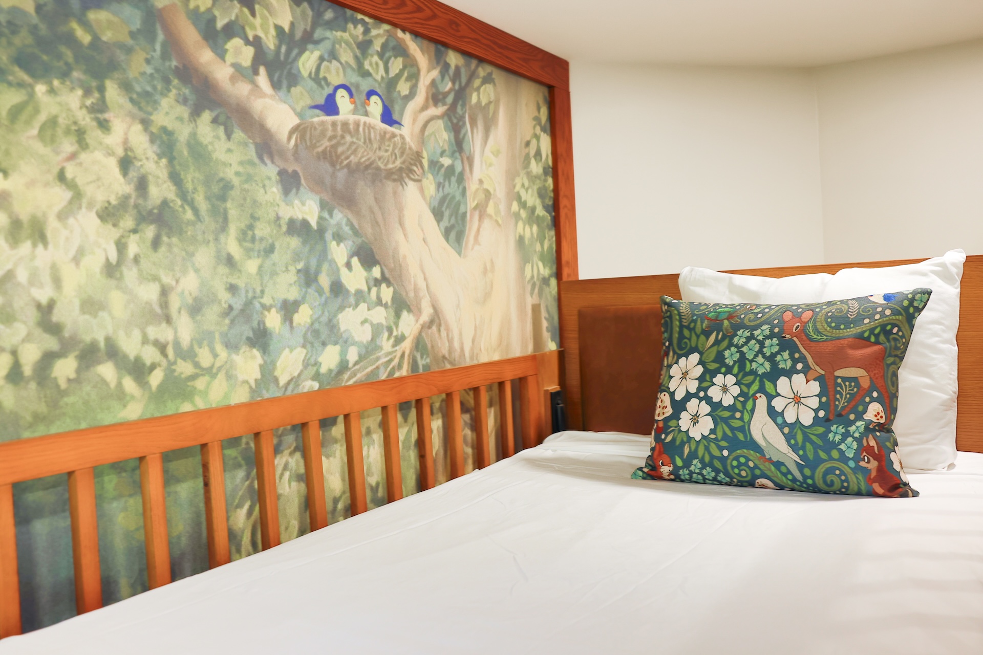 Cozy bed with decorative pillow and tree mural in background.