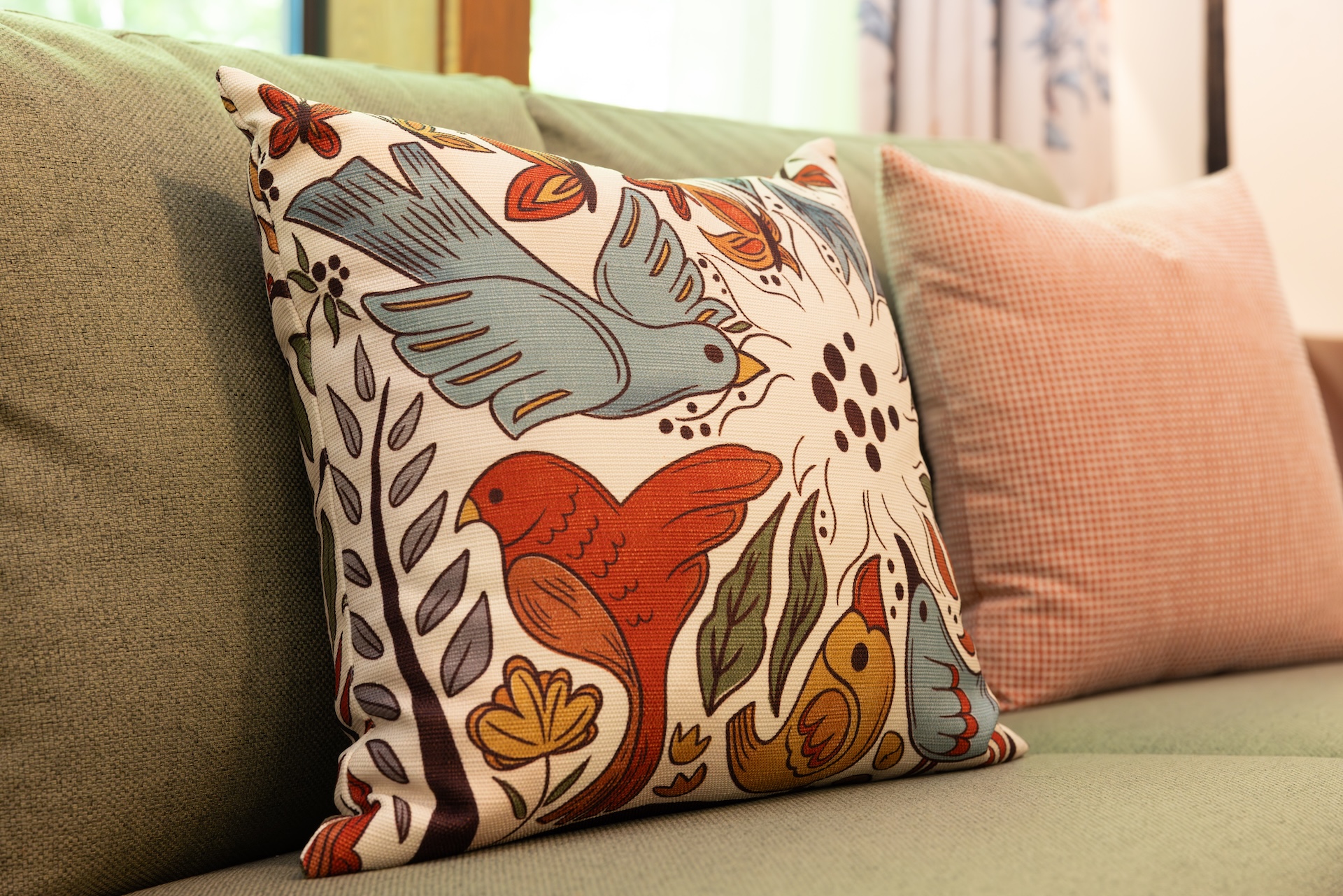 Decorative pillow with colorful birds and floral patterns on a sofa.
