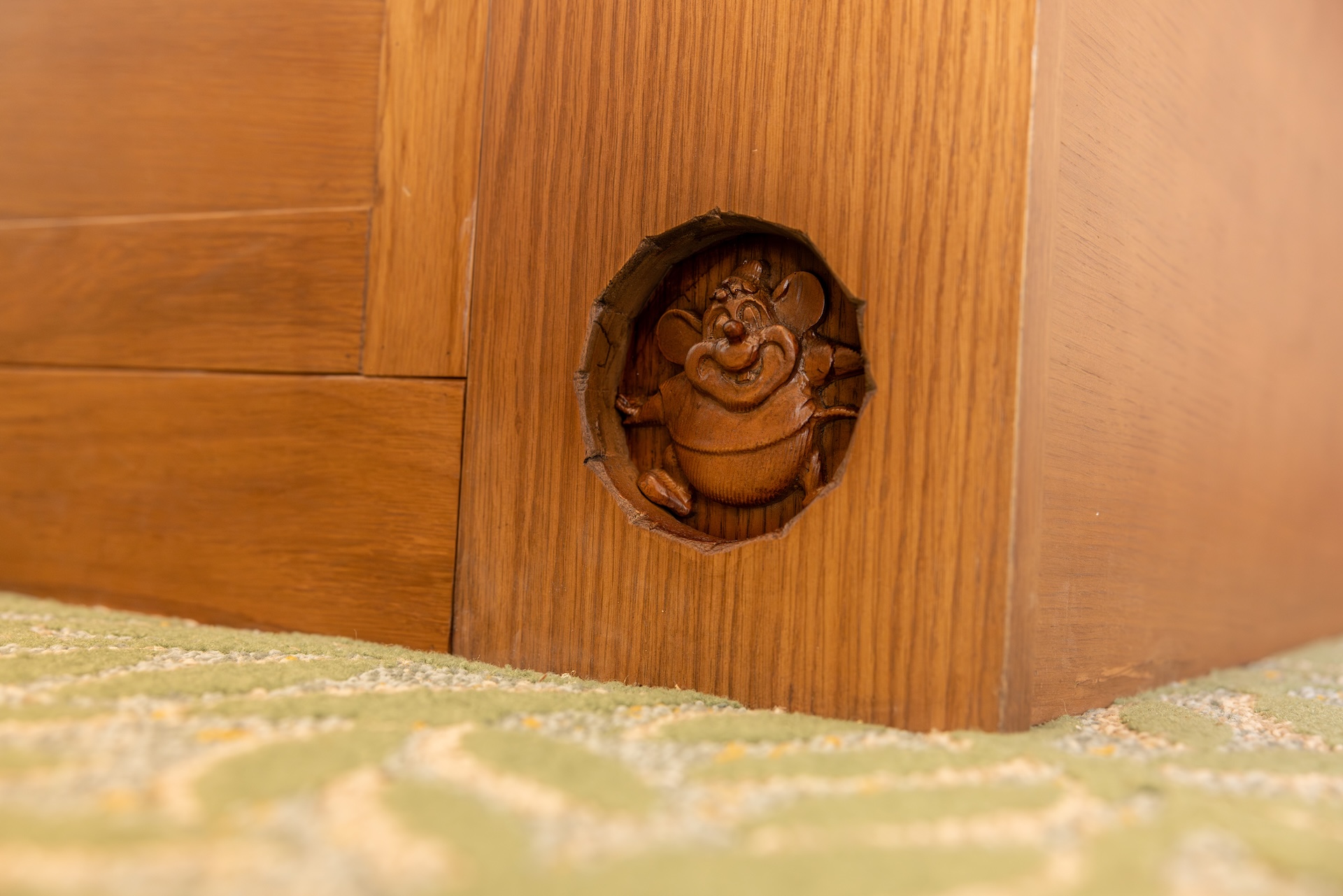 Carved wooden figure embedded in a wooden panel near a patterned carpet.