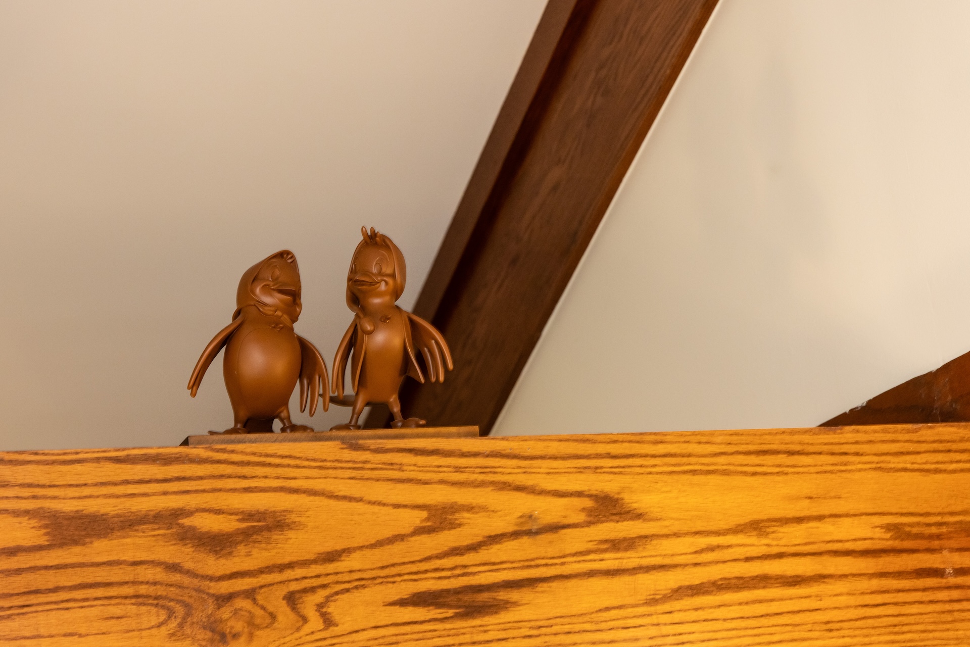 Two brown figurines of birds perched on a wooden shelf.