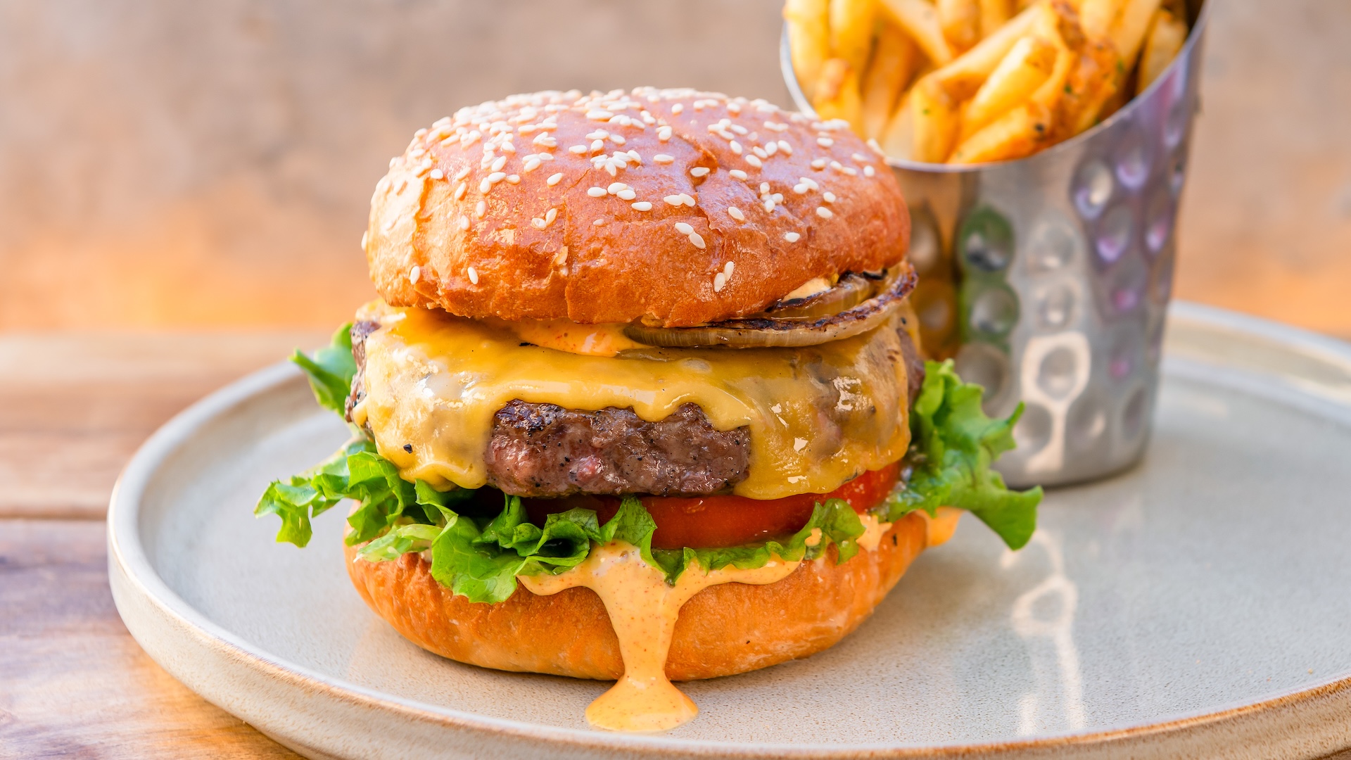 Disney Parks America 250 Foodie Guide Charbroiled Cheddar Burger: Lettuce, house pickles, tomato, grilled onions, and Lamplight spread on a sesame bun served with seasoned fries