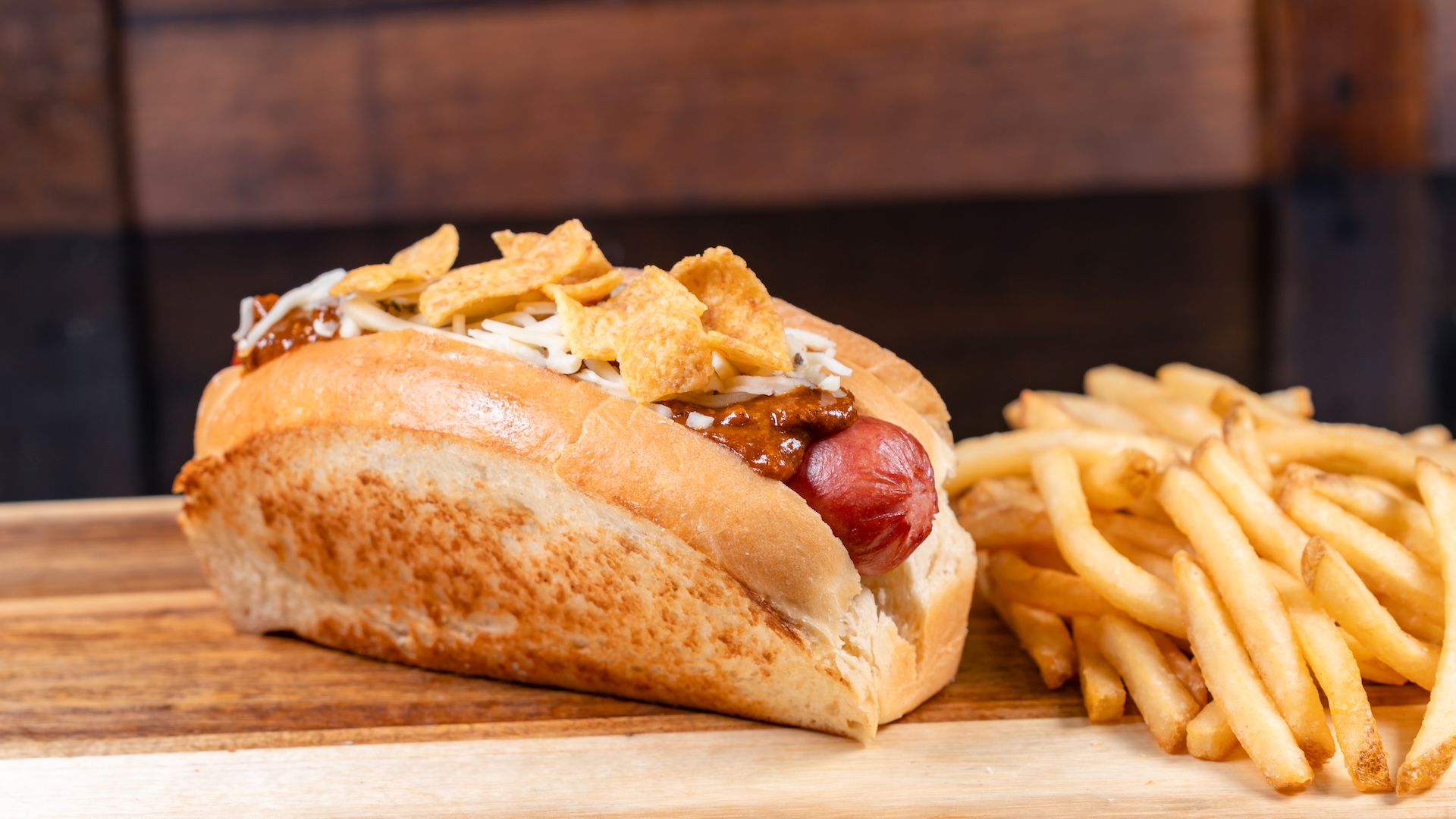 Disney Parks America 250 Foodie Guide Uptown Chili Dog: All-beef hot dog topped with home-style chili, pepper jack cheese, and corn chips served on a toasted bun with Cuties Mandarin Oranges or fries