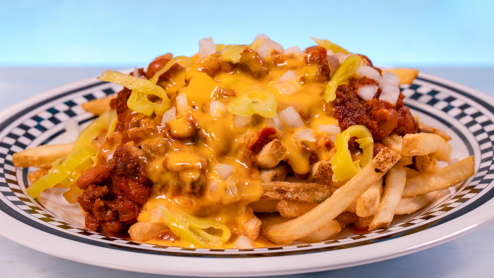 Disney Parks America 250 Foodie Guide Fast Track Loaded Fries: Fries topped with hearty chili, pepperoncini cheese sauce, sliced pepperoncini, and diced onions