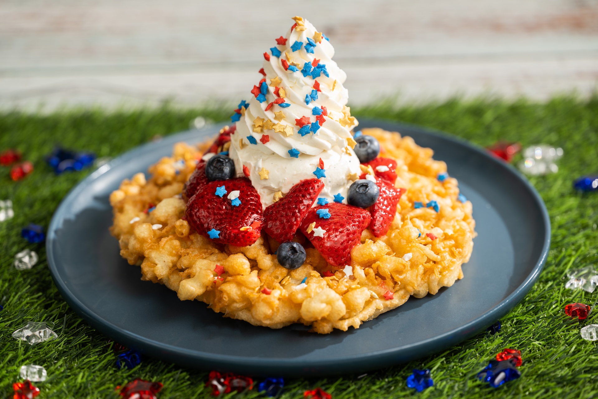 Disney Parks America 250 Foodie Guide Red, White, and Blue Funnel Cake: Funnel cake topped with mixed berries, vanilla ice cream, and festive sprinkles