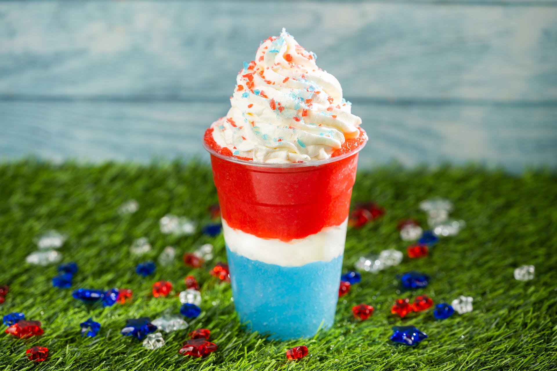 Disney Parks America 250 Foodie Guide Red, White, and Blue Slushy: Frozen Fanta Blue Raspberry and Fanta Cherry layered with whipped cream and topped with popping candies (Non-alcoholic)