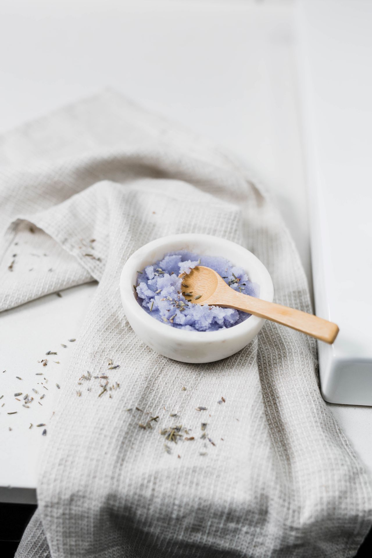 Lavender sugar scrub in a white bowl with a wooden spoon.