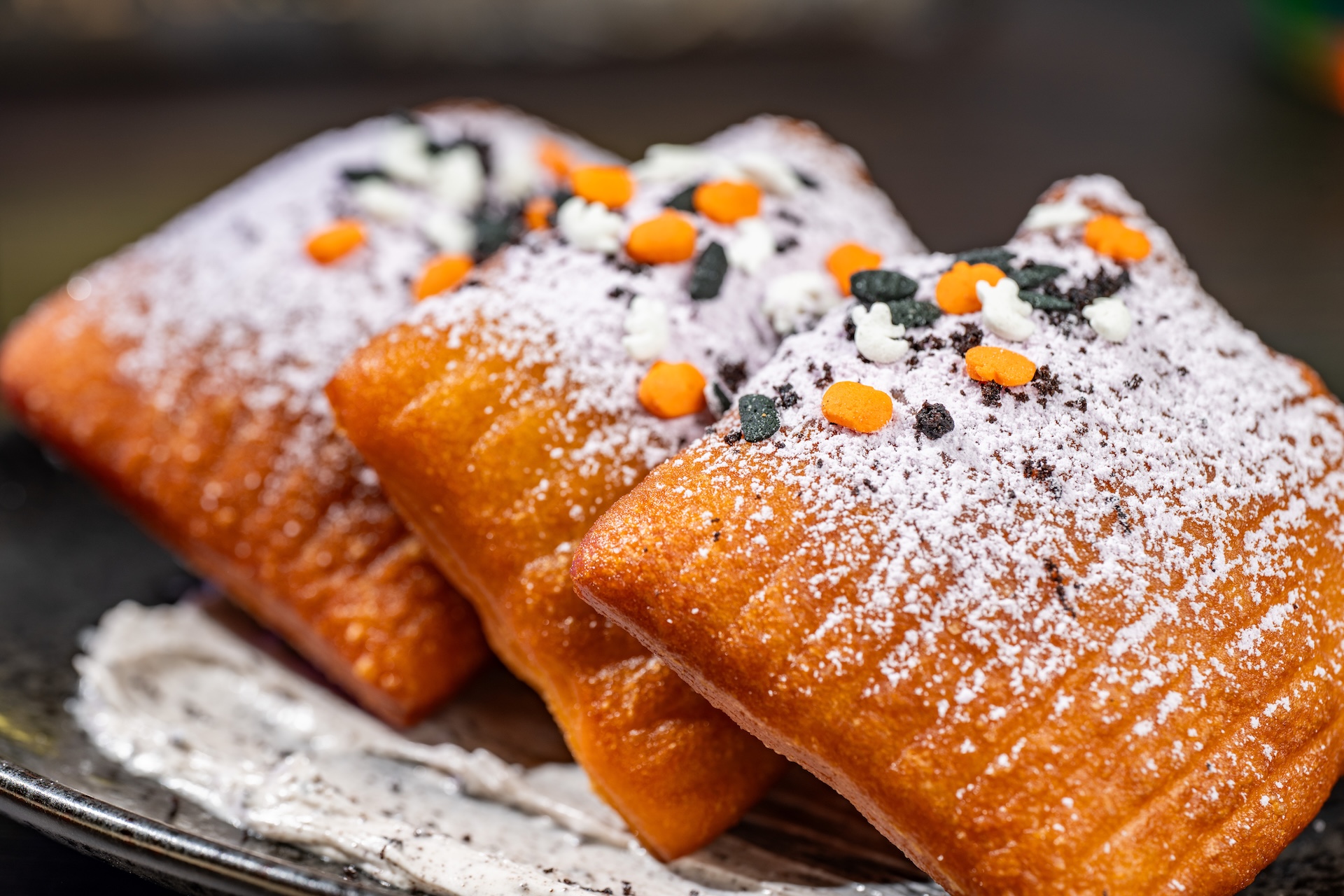 Beignets from Beyond: Light, sweet, and fluffy beignets with powdered sugar and chocolate cookie pieces over cookies and cream cheese icing (Available during Mickey&rsquo;s Not-So-Scary Halloween Party only)