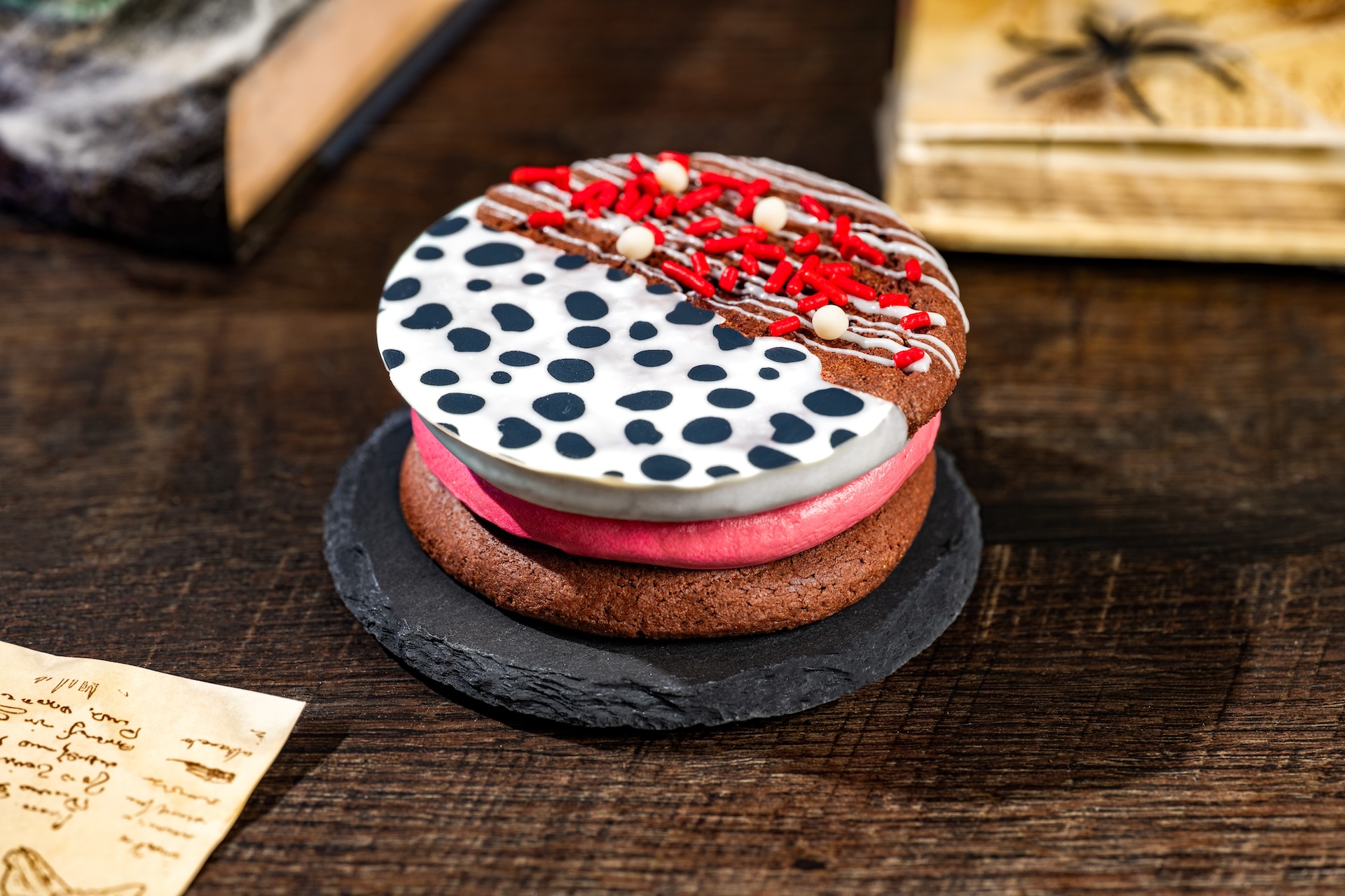 Cruella Cookie Sandwich: Chocolate cookies filled with raspberry ganache dipped in white chocolate and sprinkles (New) (Available during Mickey&rsquo;s Not-So-Scary Halloween Party only)