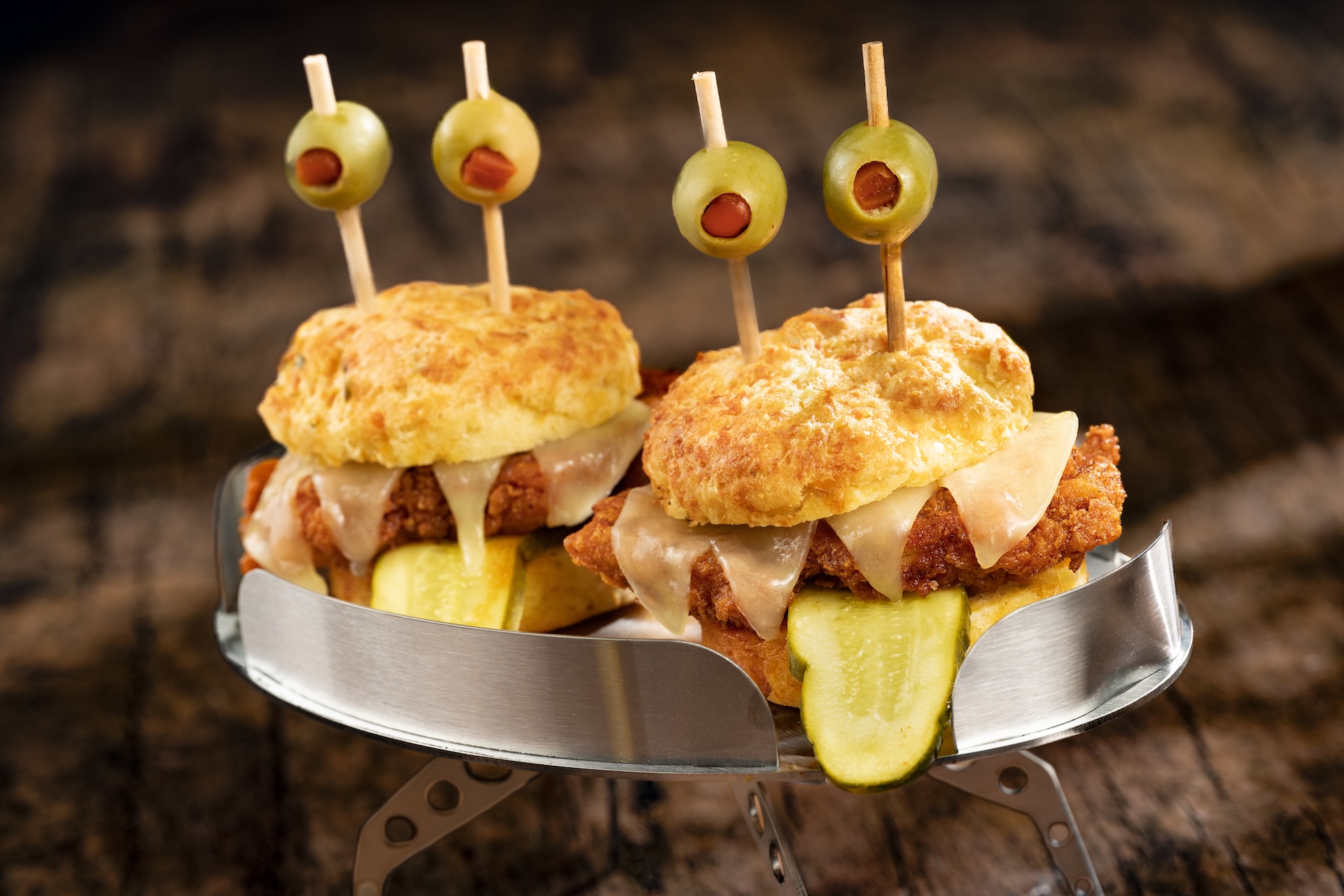 Ailen Invader Sliders: Crispy Nashville hot fried chicken, sliced provolone, dill pickle slices, cheddar-chive biscuit, and queen olives