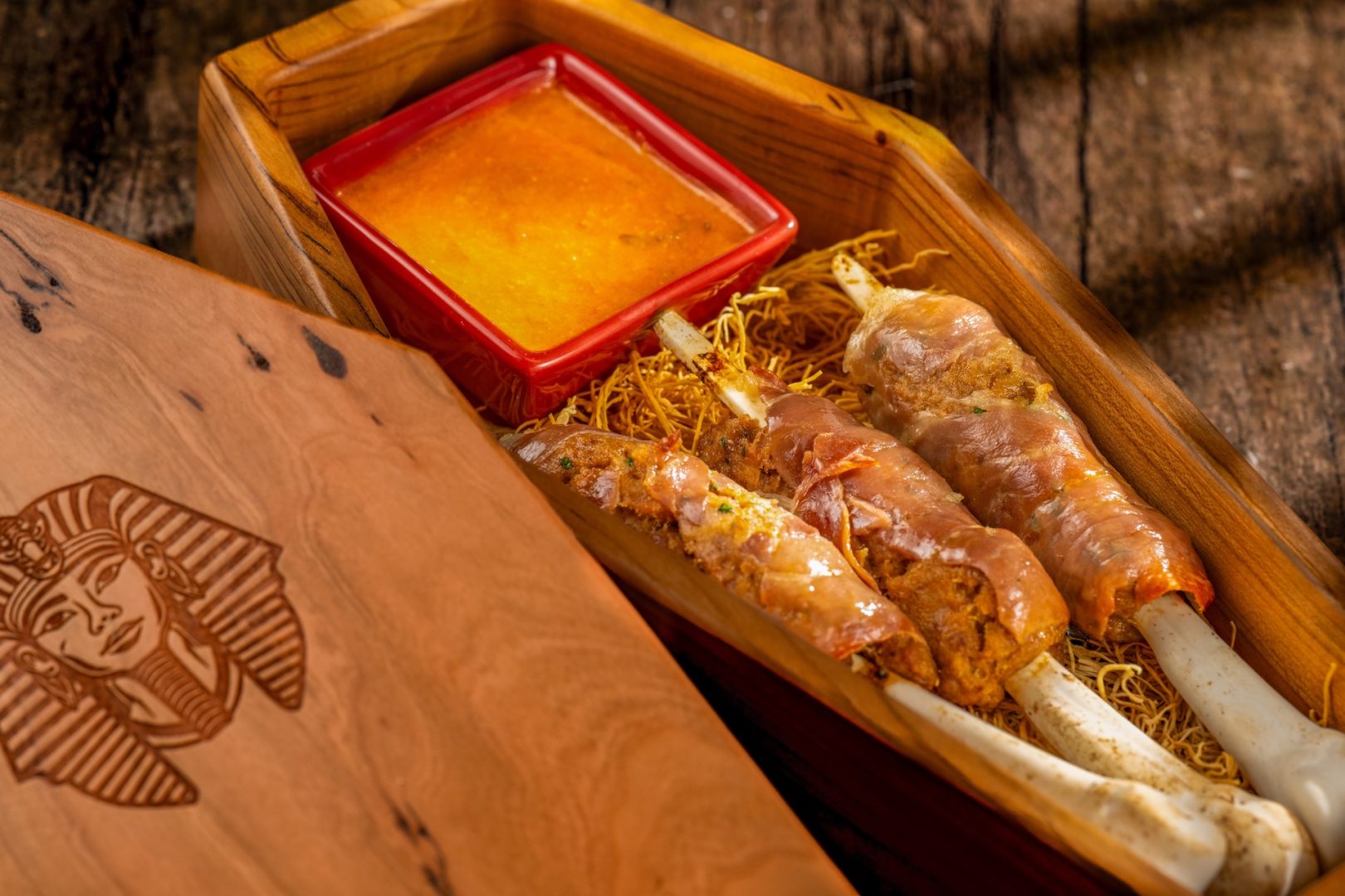 Halloween-themed food featuring skewered items and dipping sauce in a wooden tray.