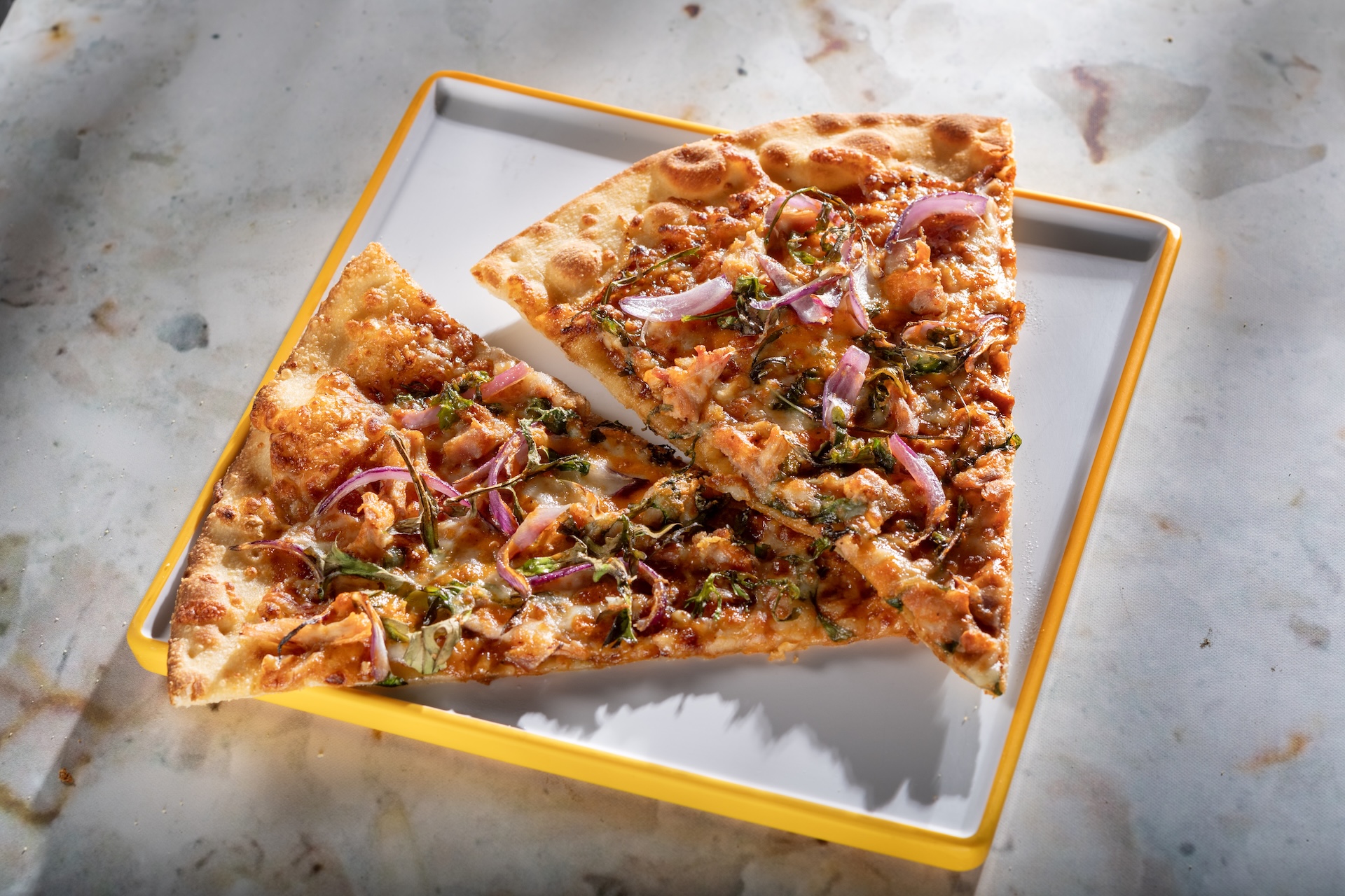 BBQ Braai Chicken Pizza: Two slices of freshly baked pizza topped with tamarind BBQ, arugula, cheese blend, onions, and piri piri sauce (New)  