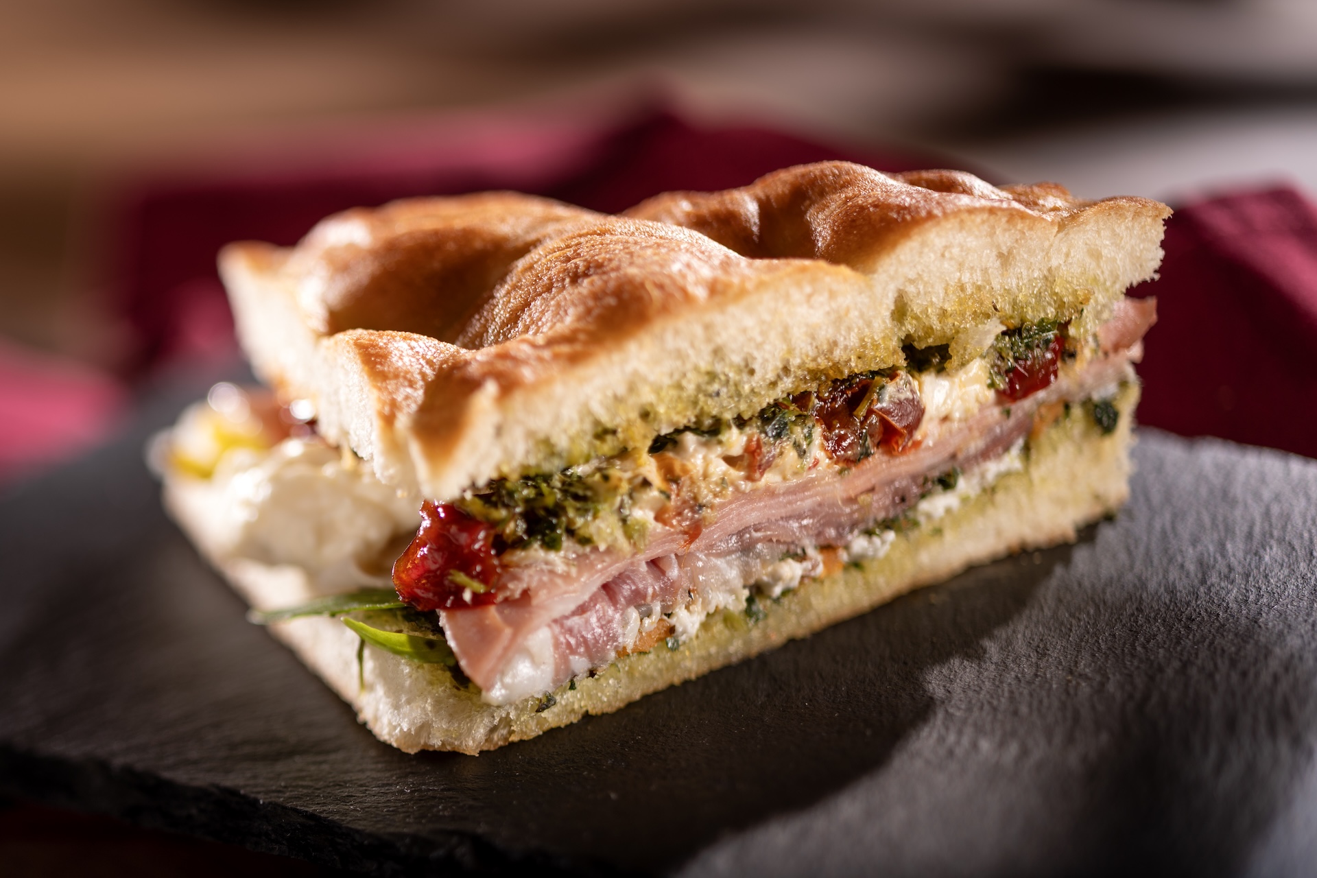 Schiacciata Sandwich: Mortadella, Prosciutto ham, sun-dried peppers, arugula, Stracciatella Cheese, fall squash mostarda, and pistachio pesto on warm focaccia  