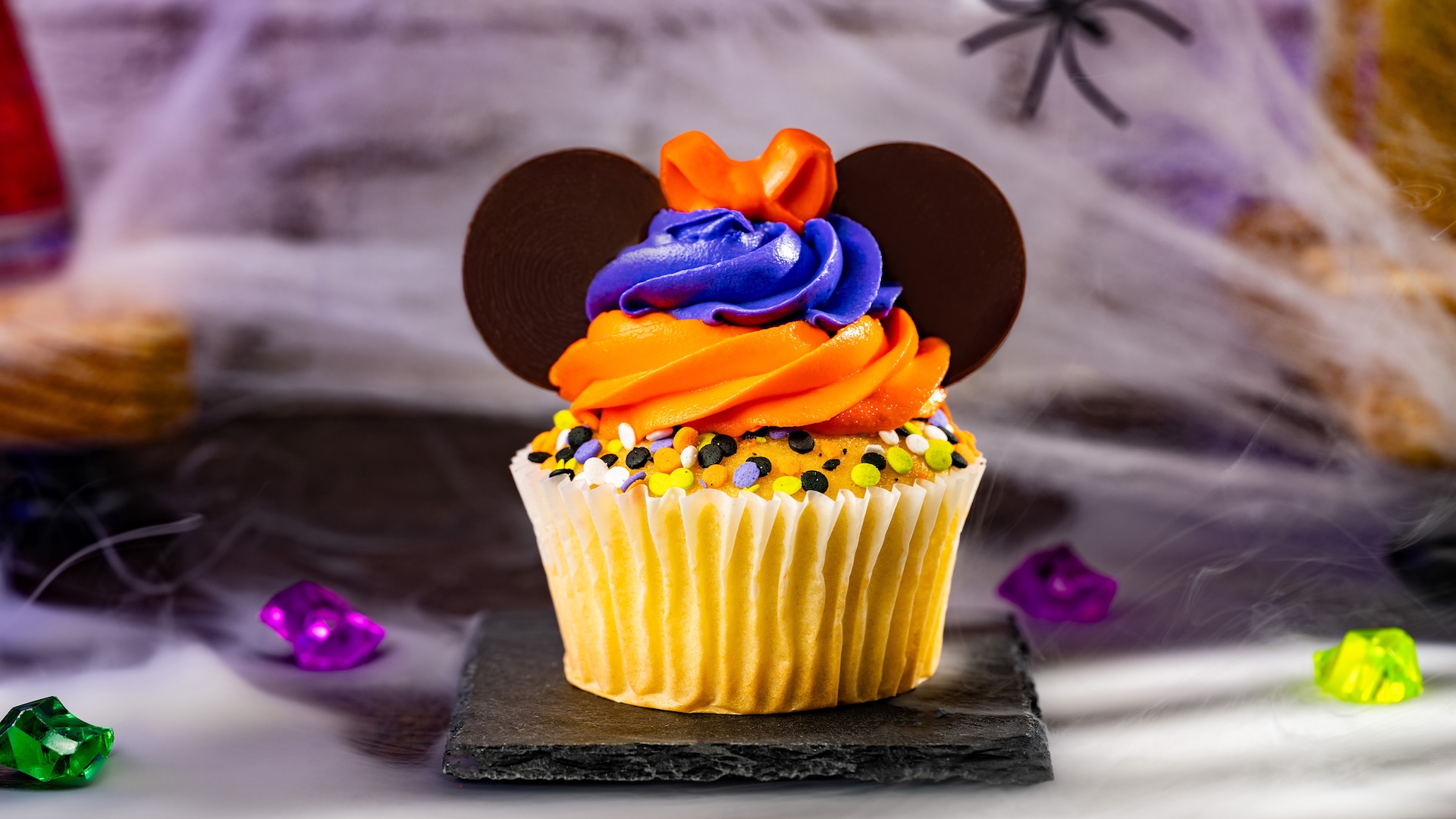 Minnie Halloween Vanilla Cupcake: Vanilla cupcake with buttercream frosting, dark chocolatey ears, Halloween sprinkles, and chocolatey bow 