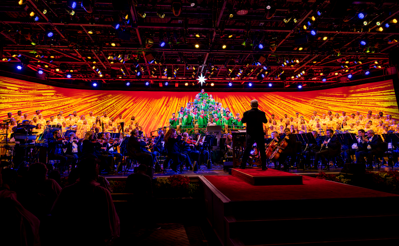 Orchestra performing with a choir in colorful stage lighting.
