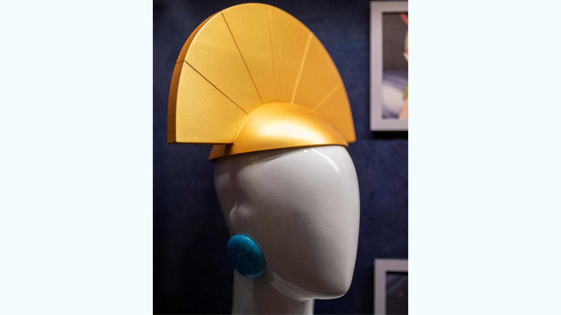 Yellow stylized headpiece displayed on a white mannequin against a dark background.