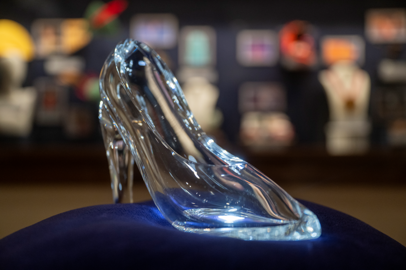 A clear glass slipper displayed on a blue velvet cushion.