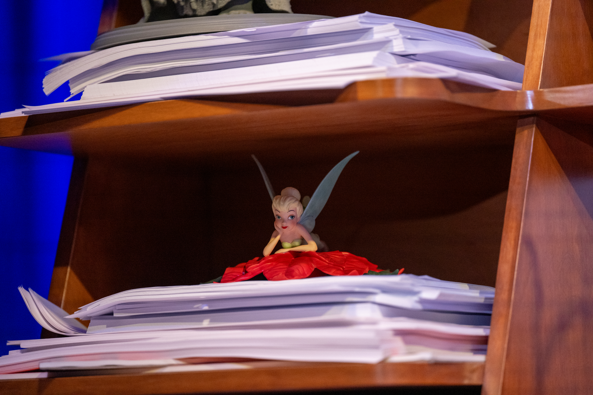 Tinker Bell figurine sitting on a pile of papers on a shelf.