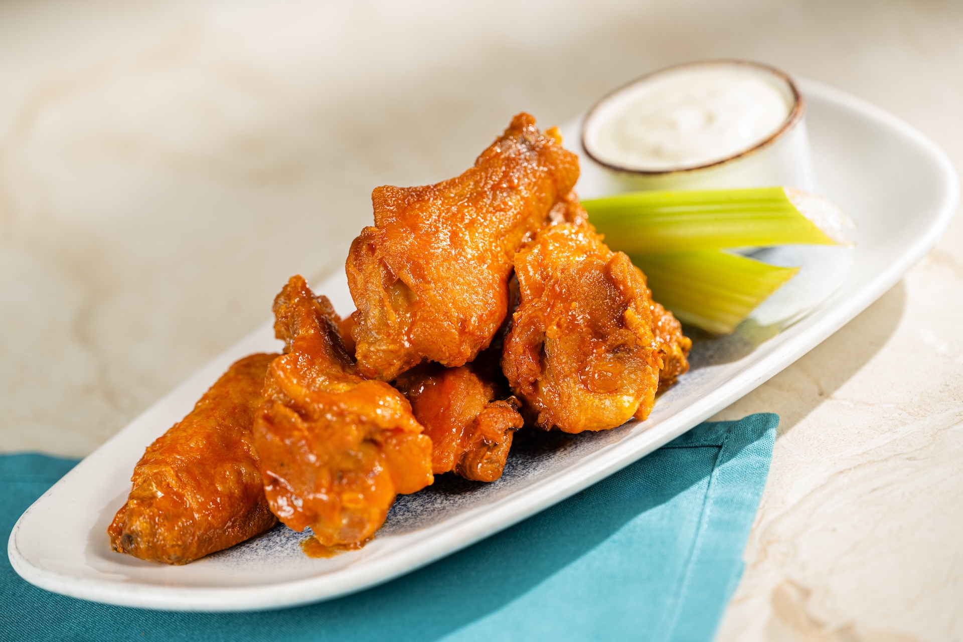 Buffalo chicken wings served with celery and dipping sauce on a plate.