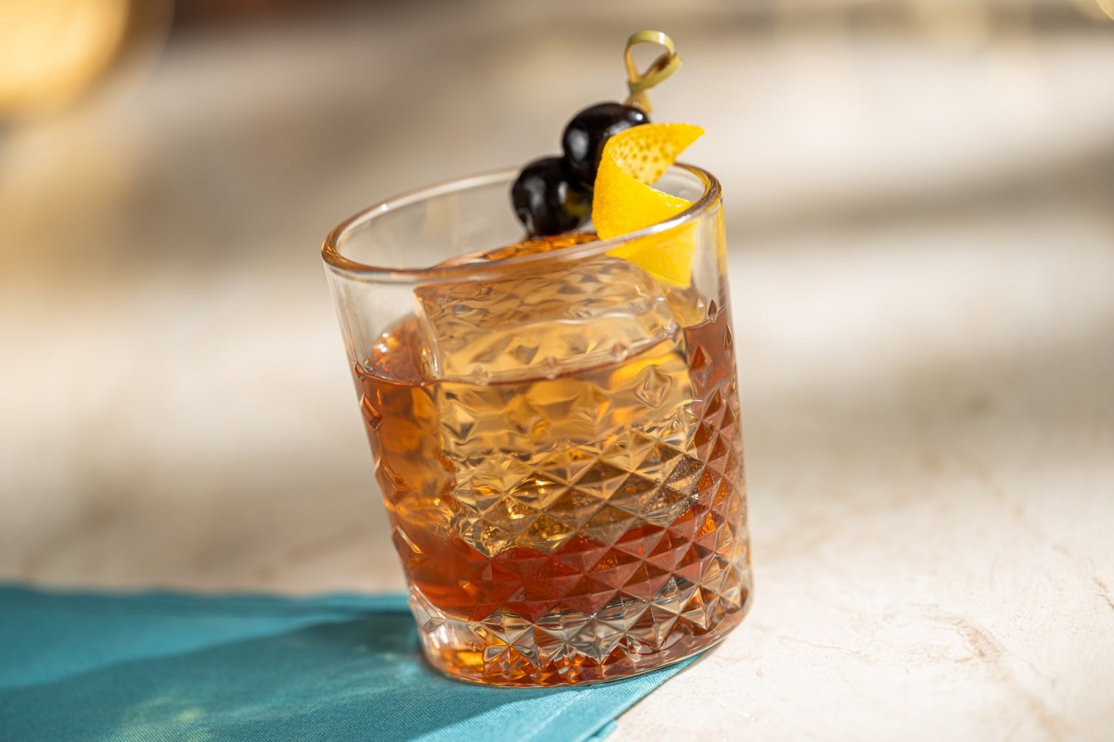Old fashioned cocktail with lemon twist and cherry garnish on a table.