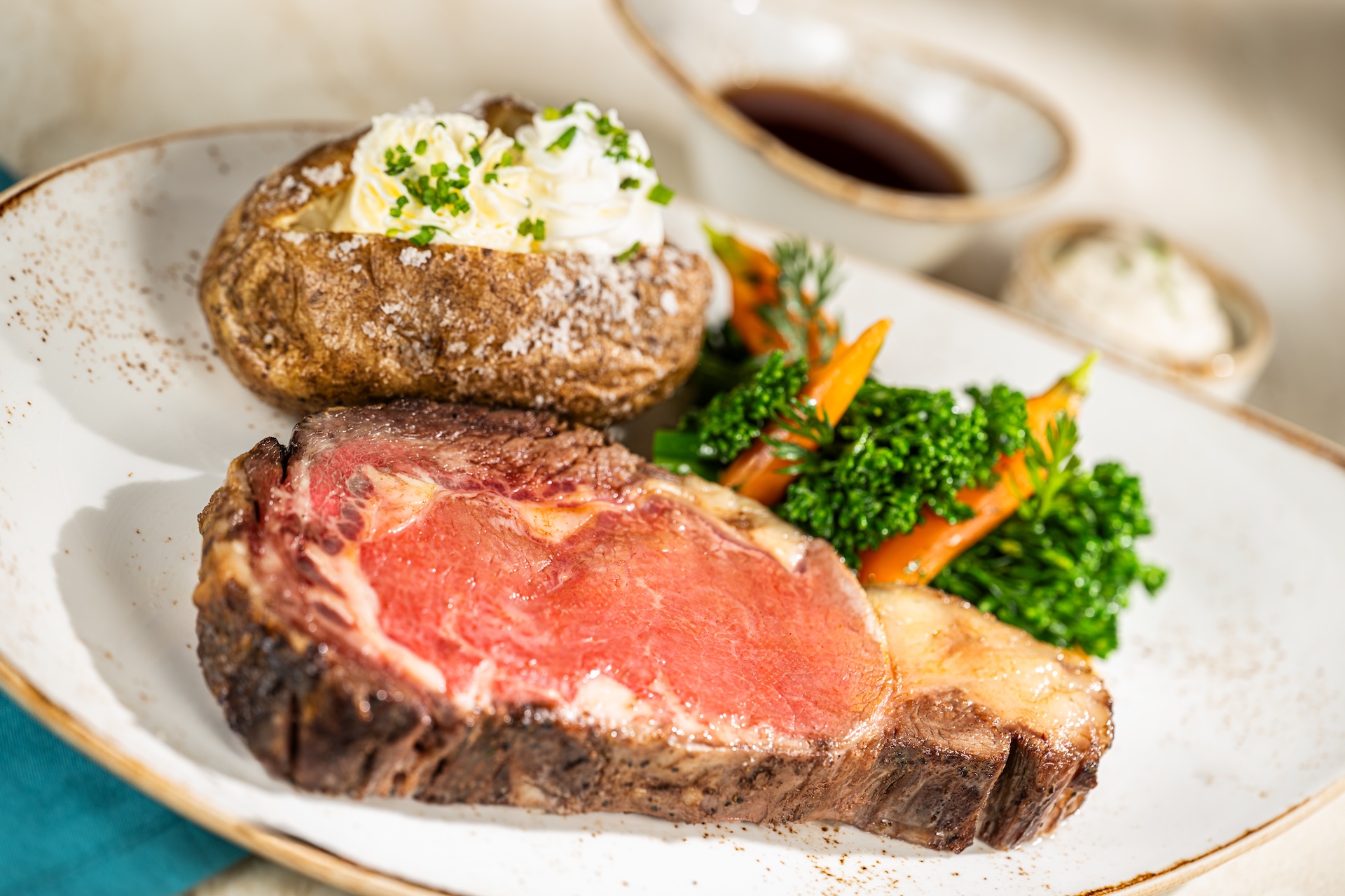 Juicy prime rib, baked potato, carrots, and broccoli on a plate.