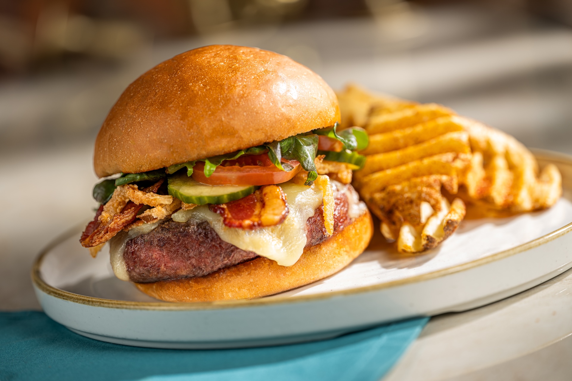 A gourmet burger with bacon, cheese, lettuce, and pickles, served with fries.